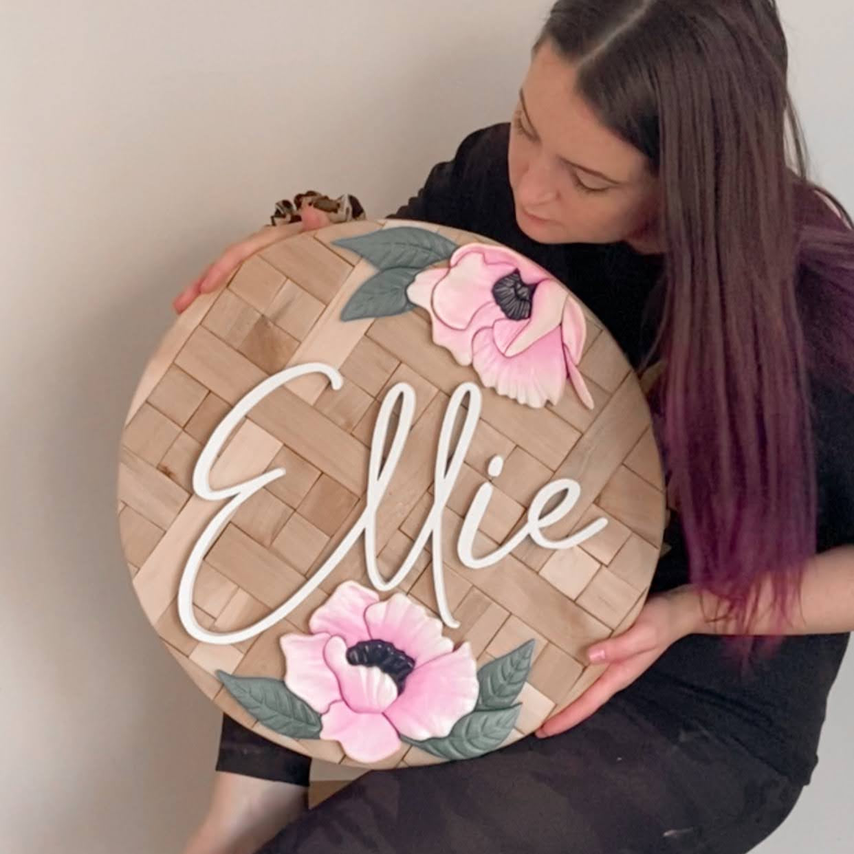 Joycelyn holding a decorative sign with 'Ellie' and floral designs